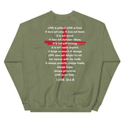 Back of military green sweater with LOVE scriptures printed and red Jesus cross in the background.